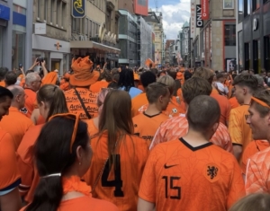 Tientallen mensen in oranje shirts gezien vanaf de rug in een straat in Dortmund