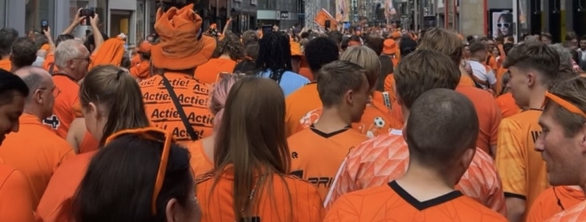 Tientallen mensen in oranje shirts gezien vanaf de rug in een straat in Dortmund